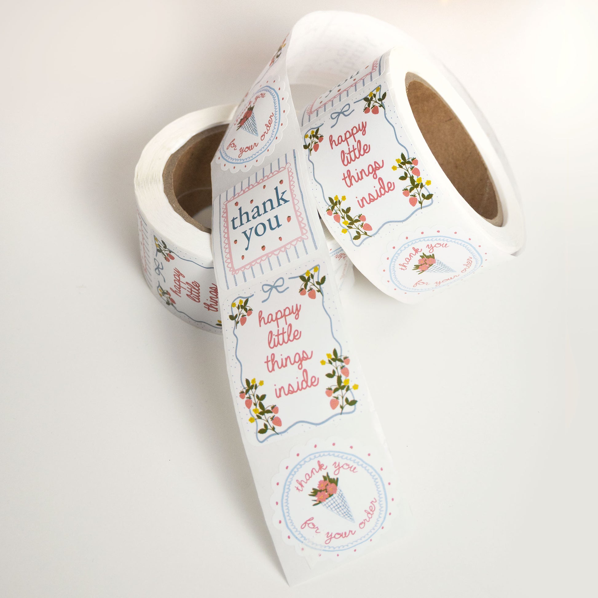 customer thank you sticker roll with three small business sticker designs in a cute, girly, coquette style of pinks and blues, strawberries, and floral designs.