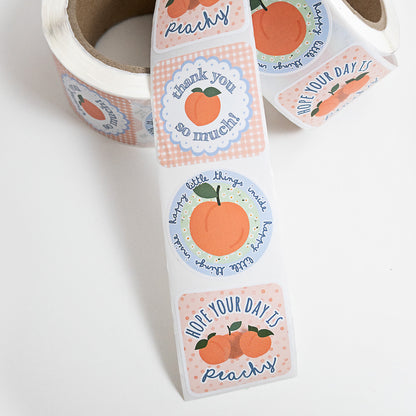 A roll of die-cut customer packaging thank you stickers with peach-themed labels, shown partially unrolled on a white background. The labels feature illustrations of peaches, gingham patterns, and handwritten text such as 'thank you so much!' and 'hope your day is peachy'